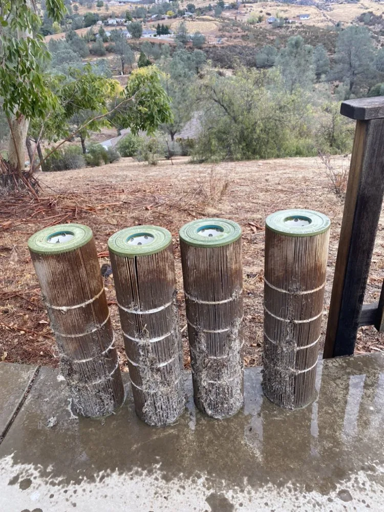 Four dirty cartridge filters standing on a wet driveway with dry hills behind