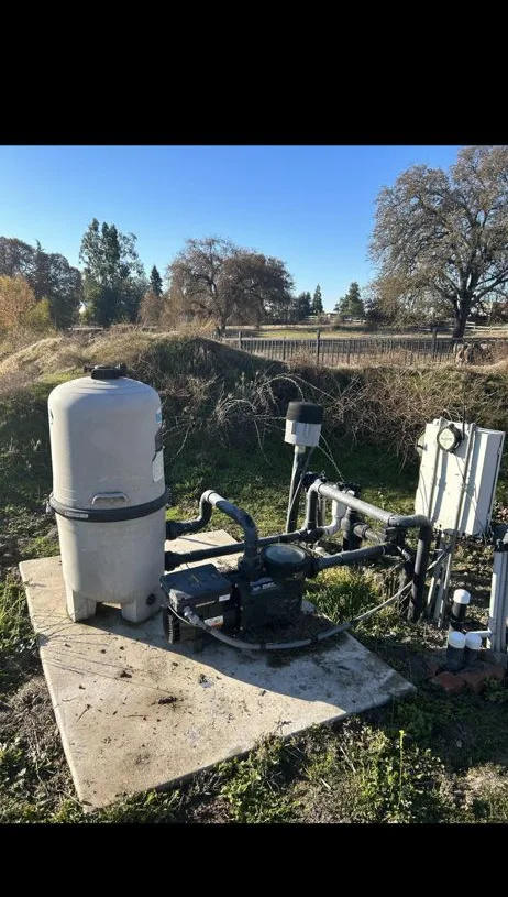 An old, weathered pool filter and pump on a dirt-edged pad