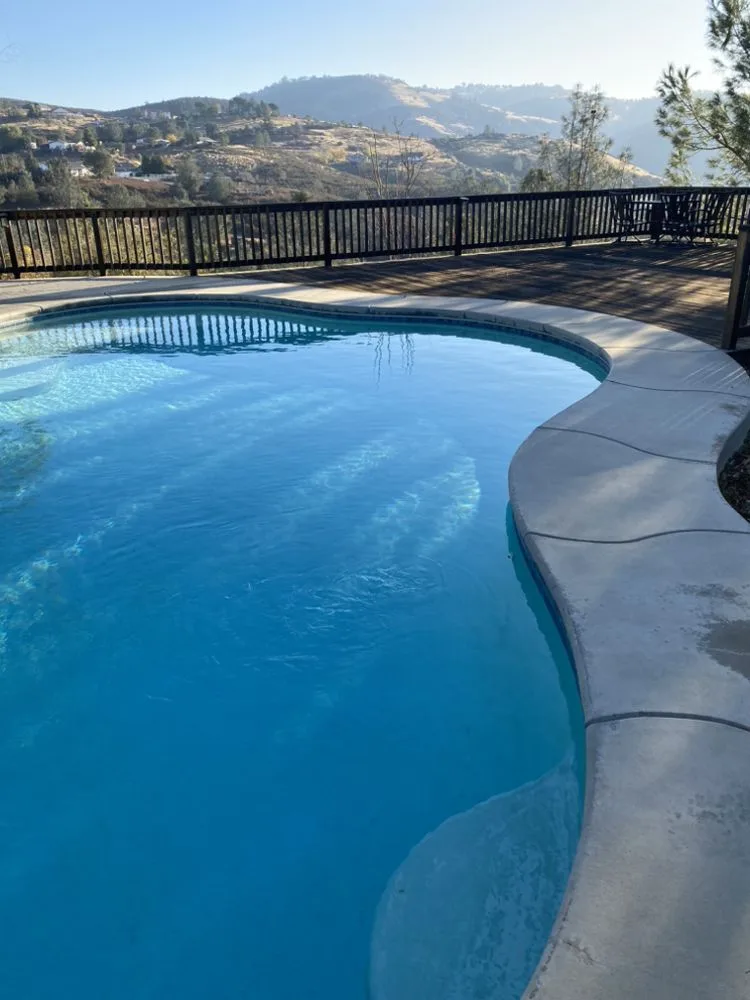 A clean blue pool on a hillside deck with a black railing, looking out over the dry Calaveras foothills