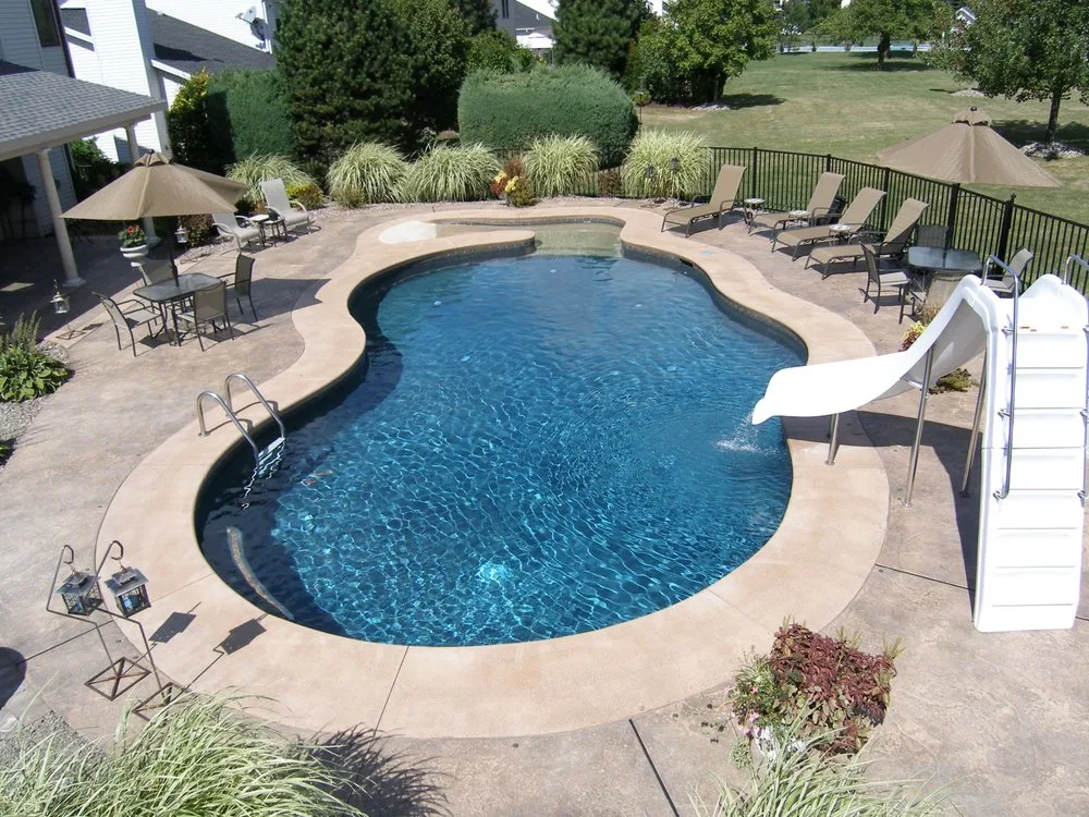 A clean kidney-shaped backyard pool with a white slide and a concrete deck